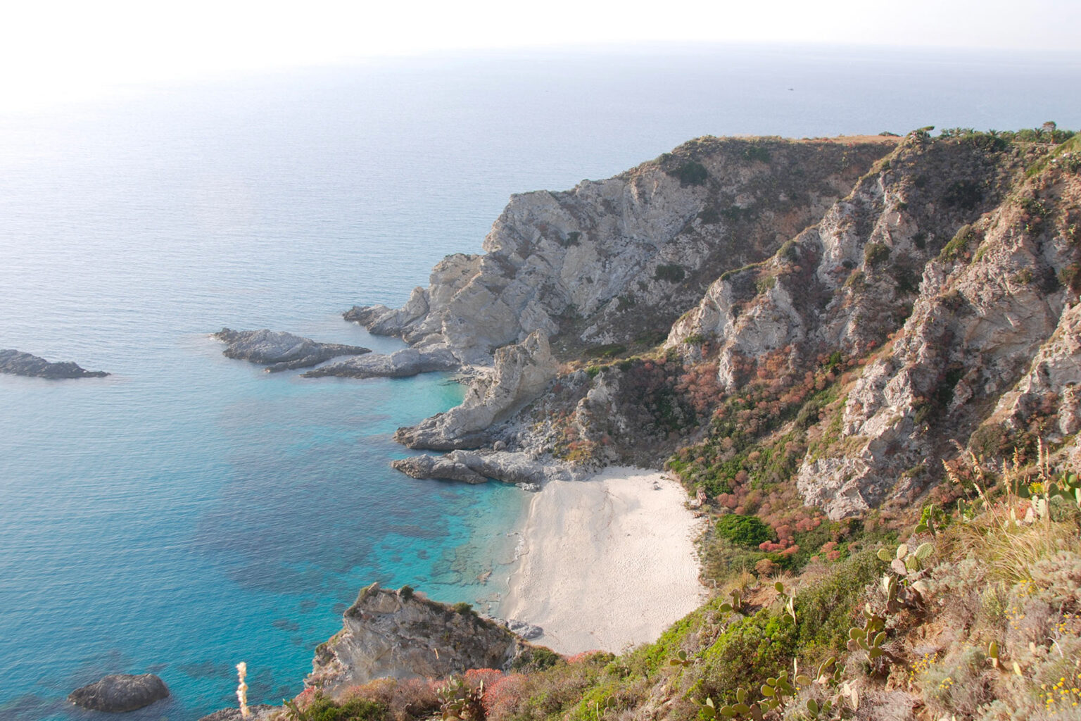 Scenic view of rugged cliffs overlooking a tranquil beach and clear blue waters, showcasing the natural beauty of the coastline. | Only on SopranoVillas