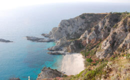 Scenic view of rugged cliffs overlooking a tranquil beach and clear blue waters, showcasing the natural beauty of the coastline.