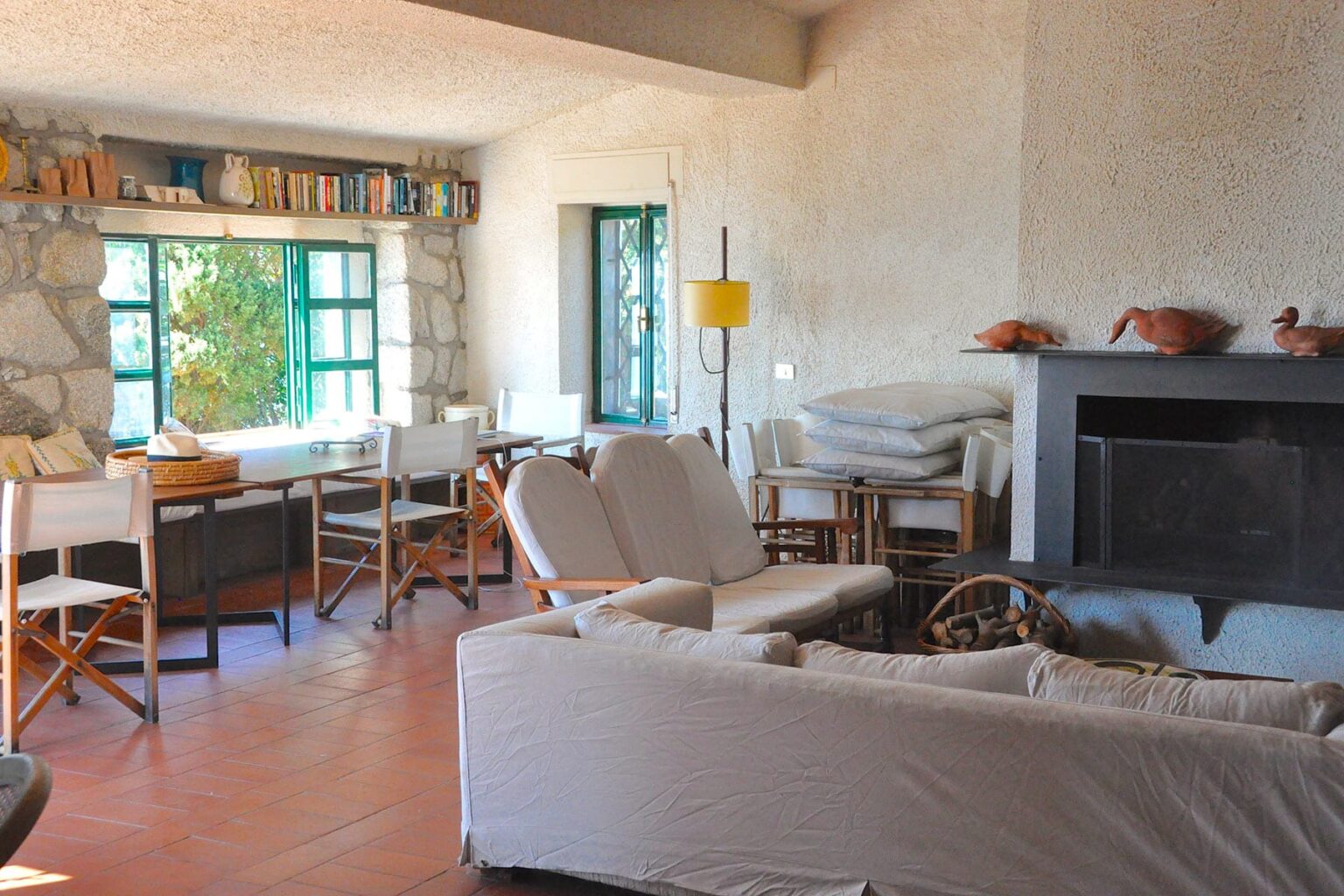Cozy living room featuring a stone wall, large windows with natural light, comfortable seating, and a rustic wooden table, creating a warm and inviting atmosphere. | Only on SopranoVillas