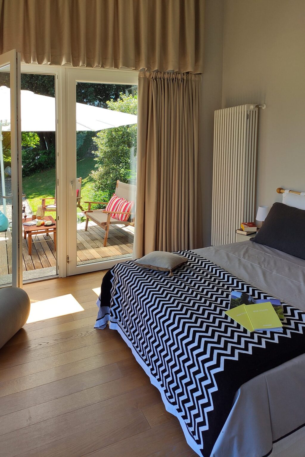 Cozy bedroom with a patterned black and white blanket, featuring a comfortable bed and large glass doors opening to a sunny outdoor patio with seating. | Only on SopranoVillas