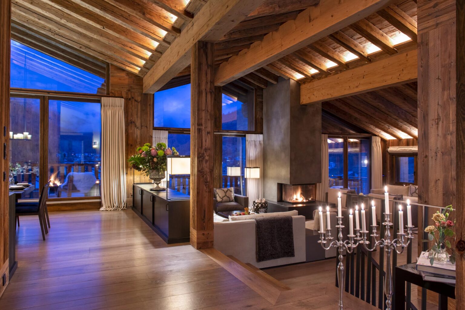Luxurious mountain lodge interior featuring wooden beams, large windows with a scenic view, elegant furnishings, and a cozy fireplace, creating a warm and inviting atmosphere. | Only on SopranoVillas