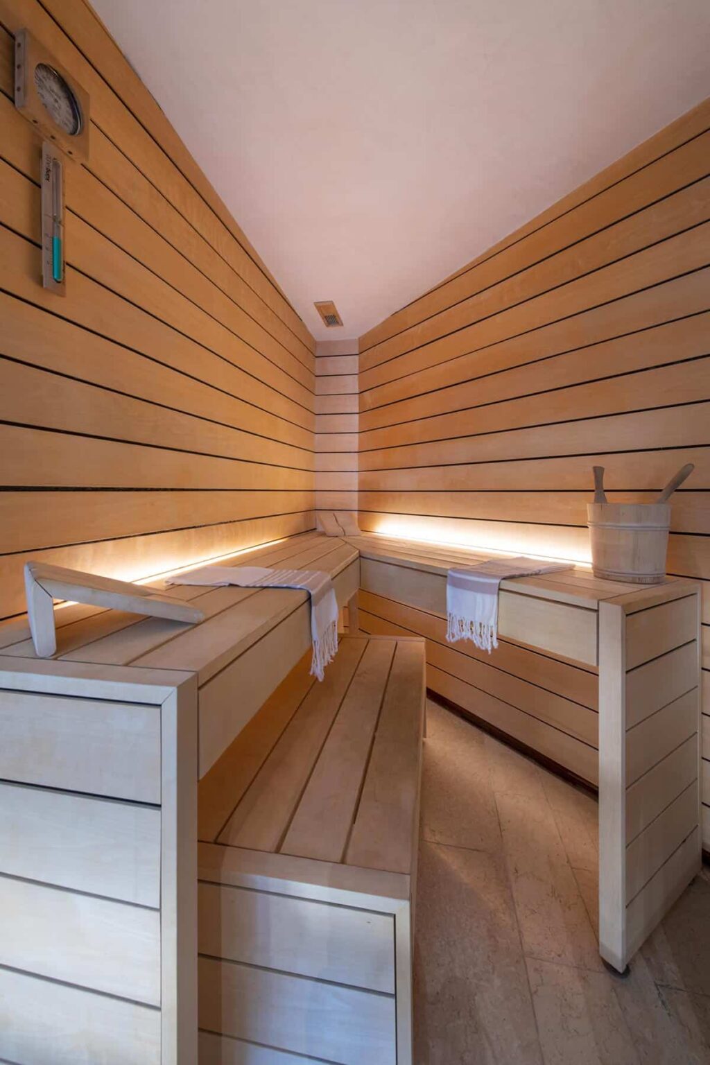Modern wooden sauna interior featuring benches, soft lighting, and a wooden bucket, ideal for relaxation and wellness. | Only on SopranoVillas