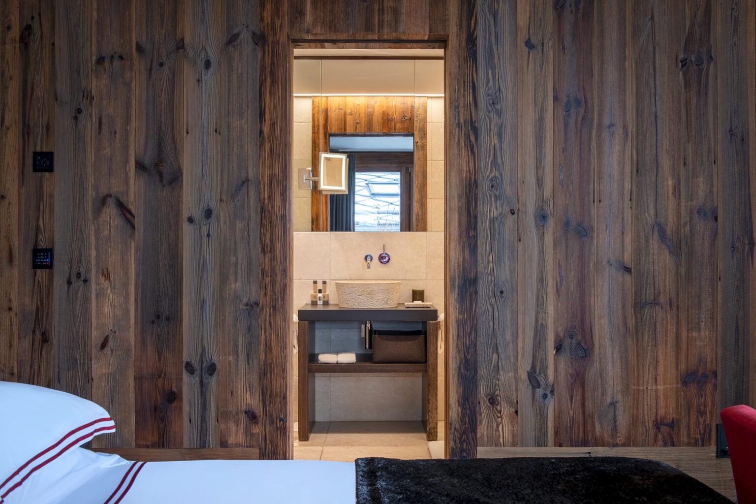 Interior view of a cozy wooden bedroom with a doorway leading to a modern bathroom, featuring warm lighting and stylish fixtures. | Only on SopranoVillas