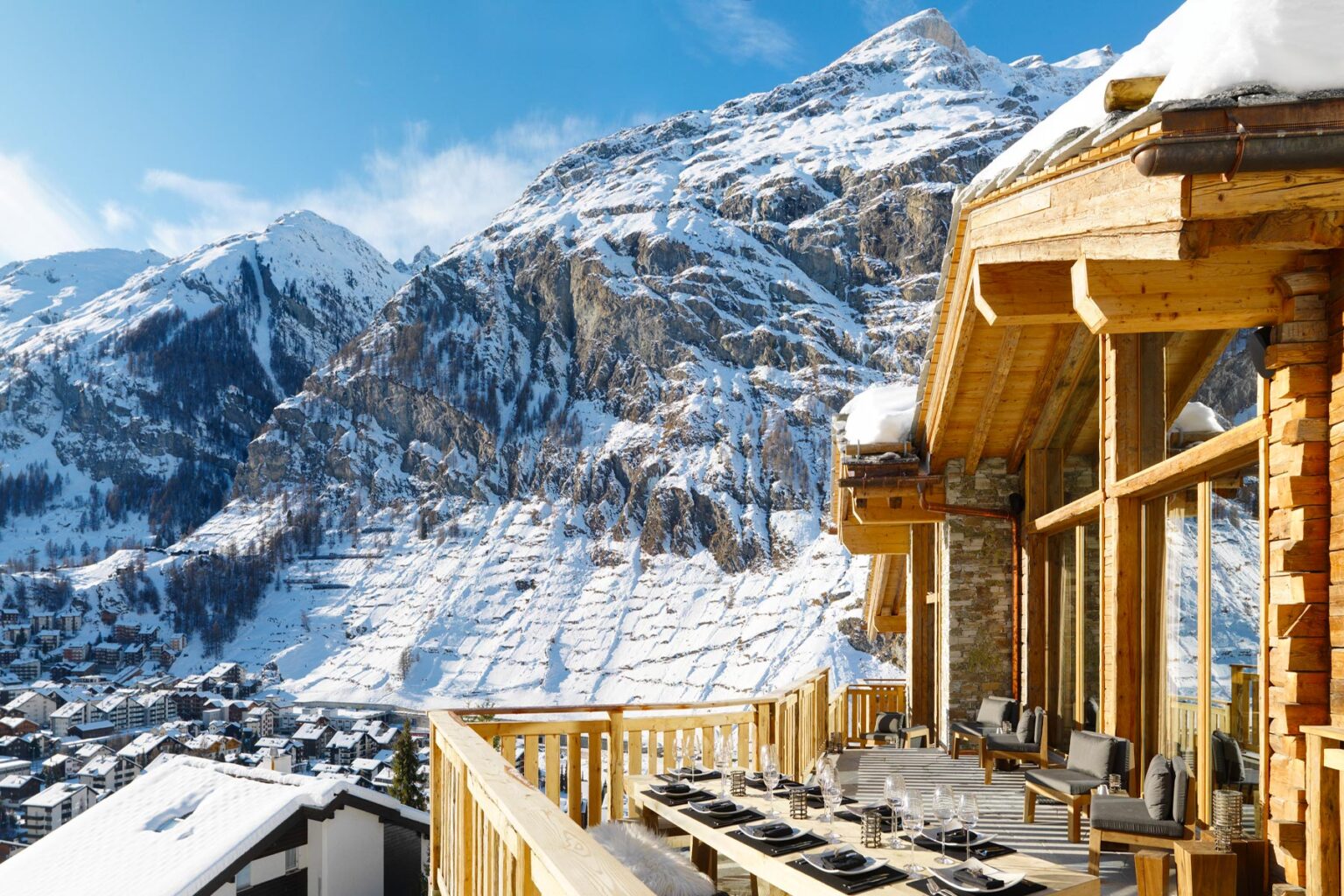 Scenic mountain view from a wooden balcony, showcasing snow-covered peaks and a picturesque village below, ideal for winter getaway and alpine retreats. | Only on SopranoVillas