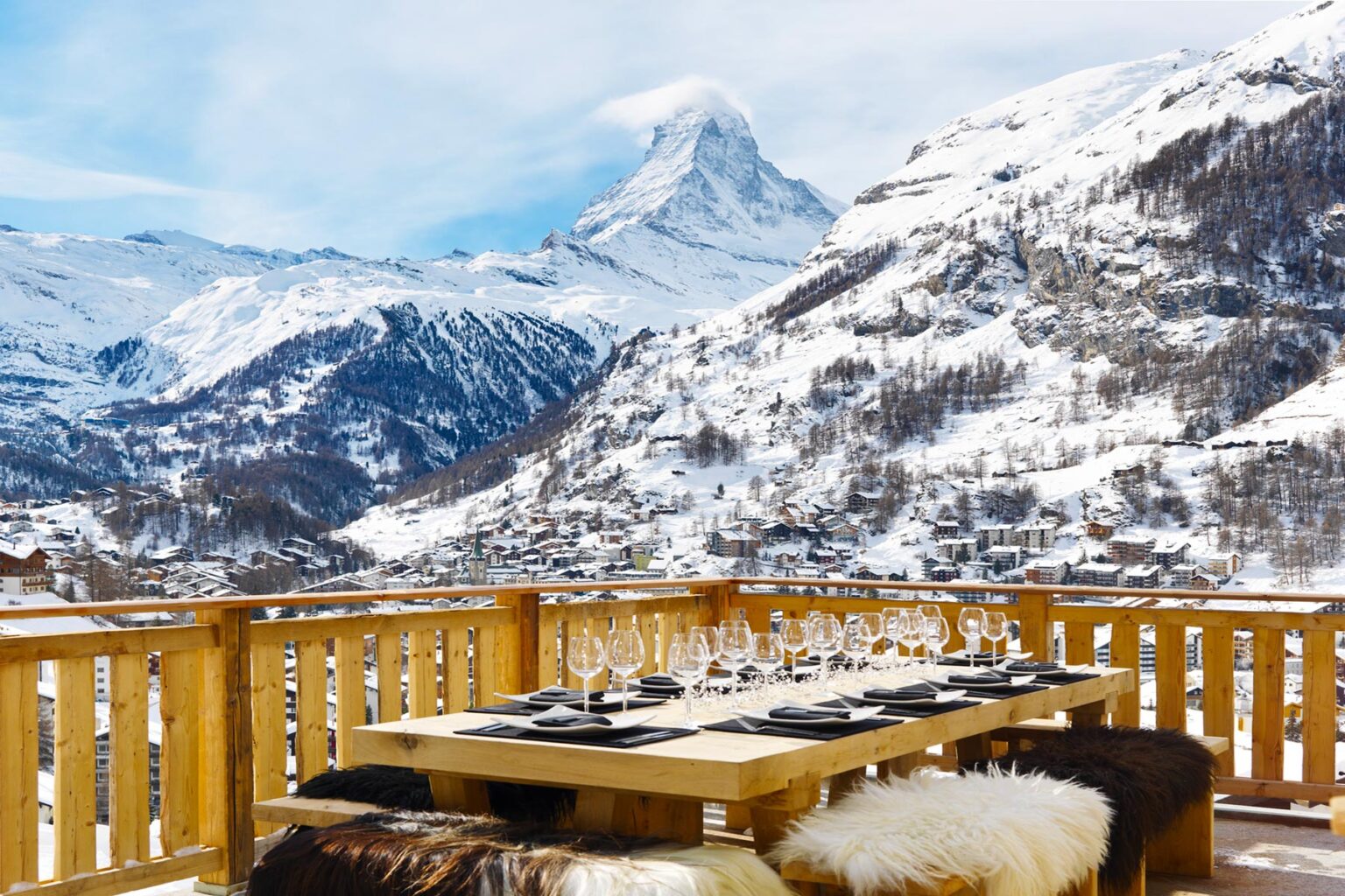 Scenic winter view from a wooden terrace overlooking snow-covered mountains, featuring a beautifully set dining table with elegant tableware and the iconic Matterhorn in the background. | Only on SopranoVillas