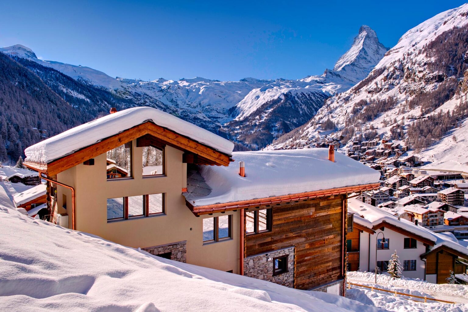 Snow-covered chalet in the Swiss Alps with a backdrop of the Matterhorn mountain, showcasing a picturesque winter landscape and charming alpine architecture. | Only on SopranoVillas