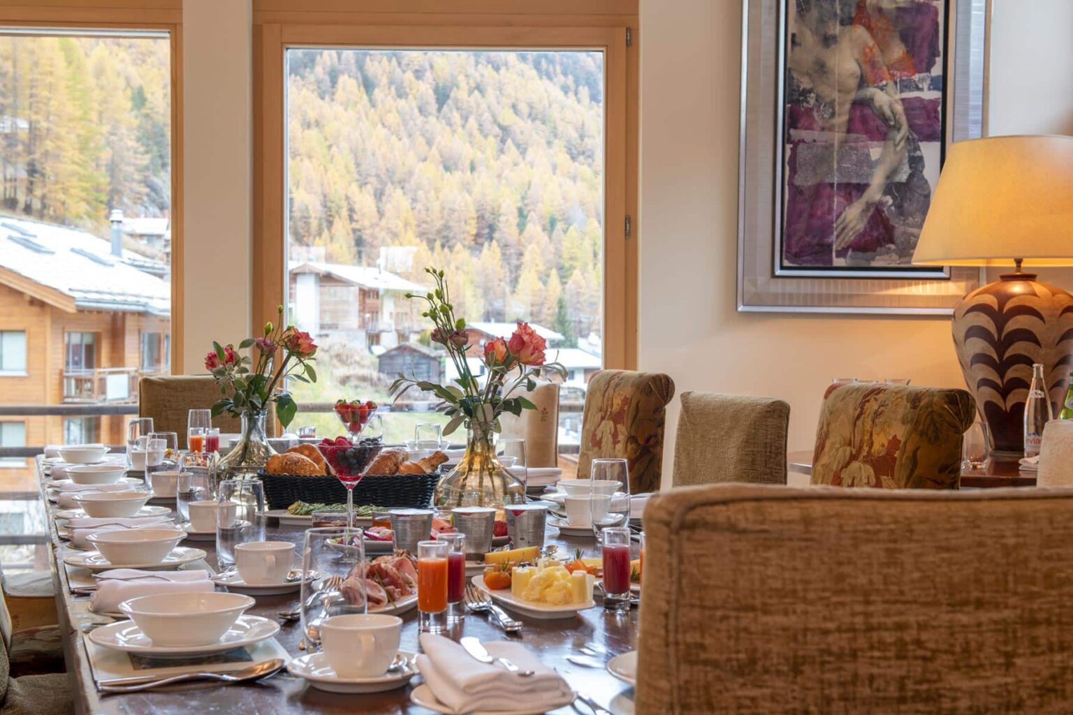 Elegant dining room set for breakfast, featuring a long table with white dishware, fresh flowers, and a view of autumn foliage outside the window. Cozy atmosphere with warm lighting and tasteful decor. | Only on SopranoVillas