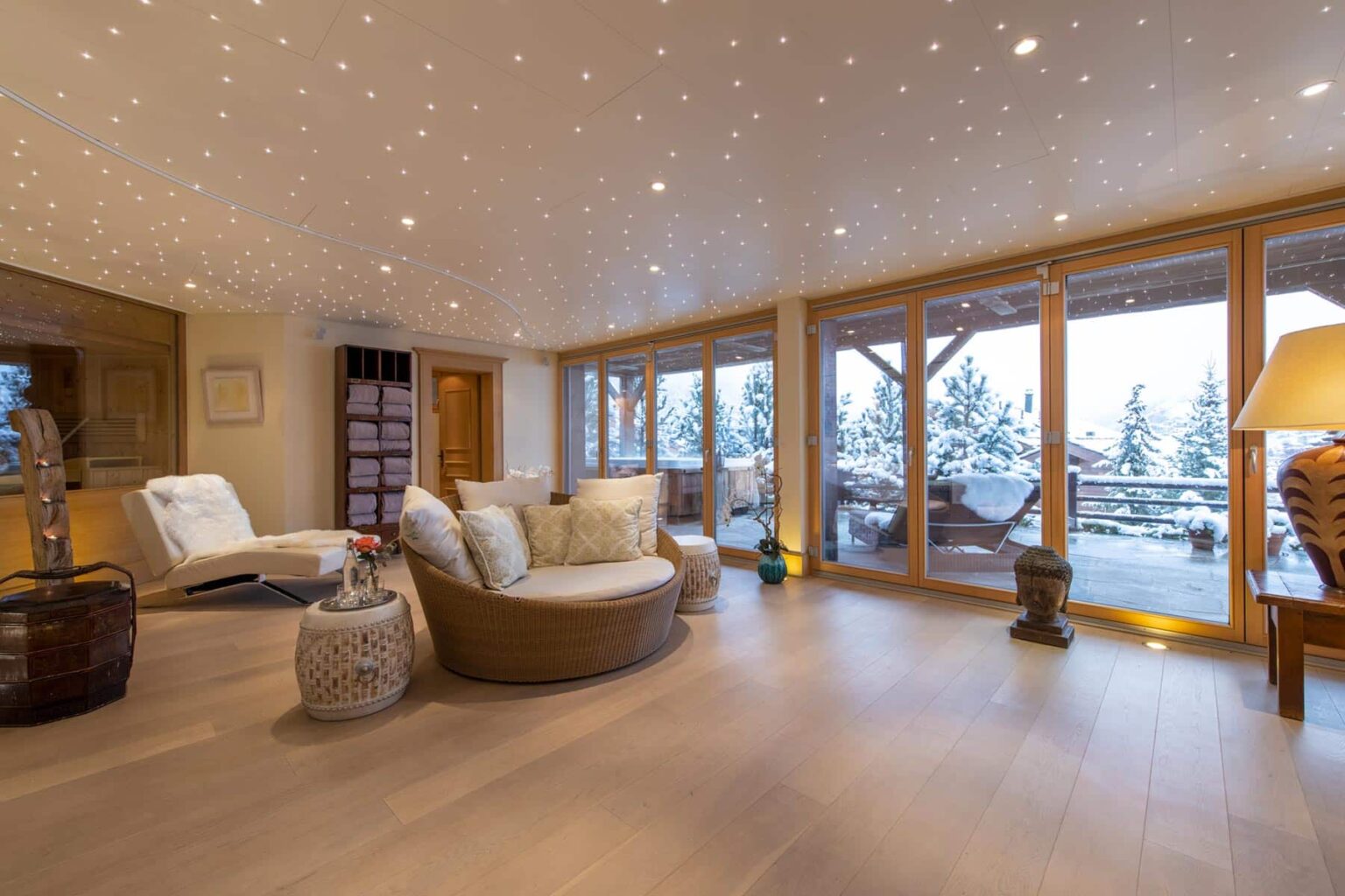 Cozy modern living room with large windows overlooking a snowy landscape, featuring comfortable seating, warm lighting, and stylish decor. Ideal for relaxation and enjoying scenic views. | Only on SopranoVillas