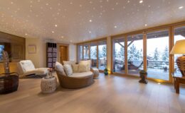 Cozy modern living room with large windows overlooking a snowy landscape, featuring comfortable seating, warm lighting, and stylish decor. Ideal for relaxation and enjoying scenic views.
