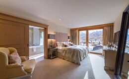 Luxurious hotel bedroom featuring a king-sized bed, elegant furnishings, and large windows showcasing a mountain view. The room includes a cozy seating area and modern amenities, creating a serene and inviting atmosphere. Perfect for a relaxing getaway.
