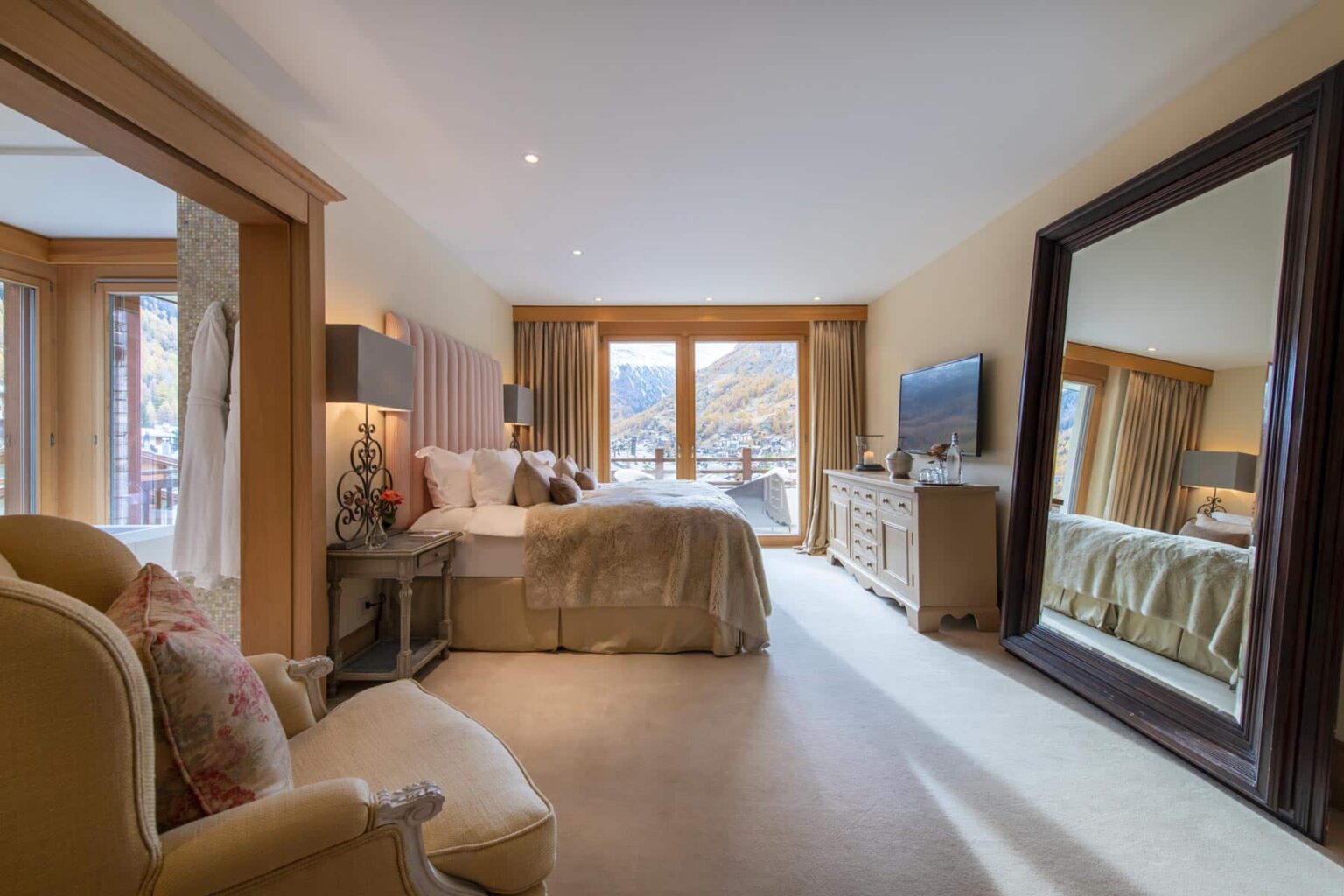 Spacious and elegantly designed bedroom featuring a large bed, stylish furnishings, and a full-length mirror, with natural light streaming through large windows that offer scenic views. | Only on SopranoVillas