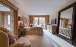 Spacious and elegantly designed bedroom featuring a large bed, stylish furnishings, and a full-length mirror, with natural light streaming through large windows that offer scenic views.
