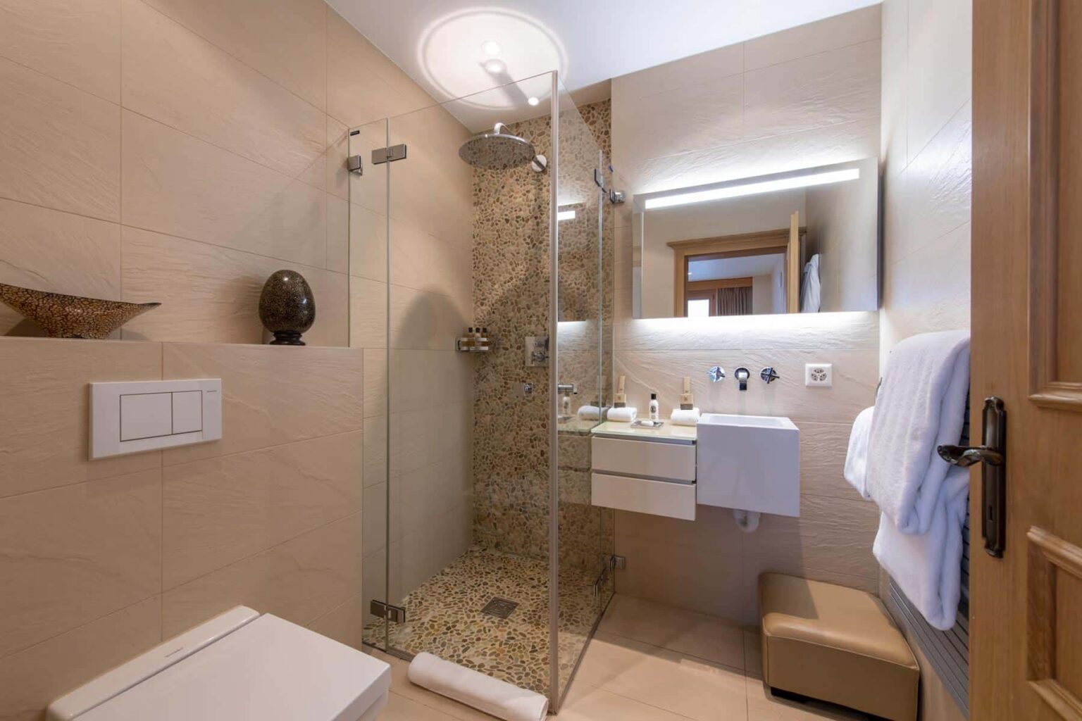 Modern bathroom featuring a glass shower, sleek vanity with sink, and neutral-toned tile decor. The space is well-lit with a contemporary design and includes a towel rack and decorative elements. | Only on SopranoVillas