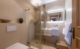 Modern bathroom featuring a glass shower, sleek vanity with sink, and neutral-toned tile decor. The space is well-lit with a contemporary design and includes a towel rack and decorative elements.