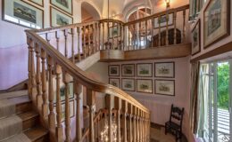 Elegant wooden staircase in a well-lit interior, adorned with framed artwork on the walls, showcasing a blend of classic design and natural light.