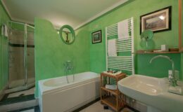 Modern bathroom featuring a green color scheme, a bathtub, a shower area, a sink with a stylish faucet, and decorative elements like framed pictures and a wooden storage rack.
