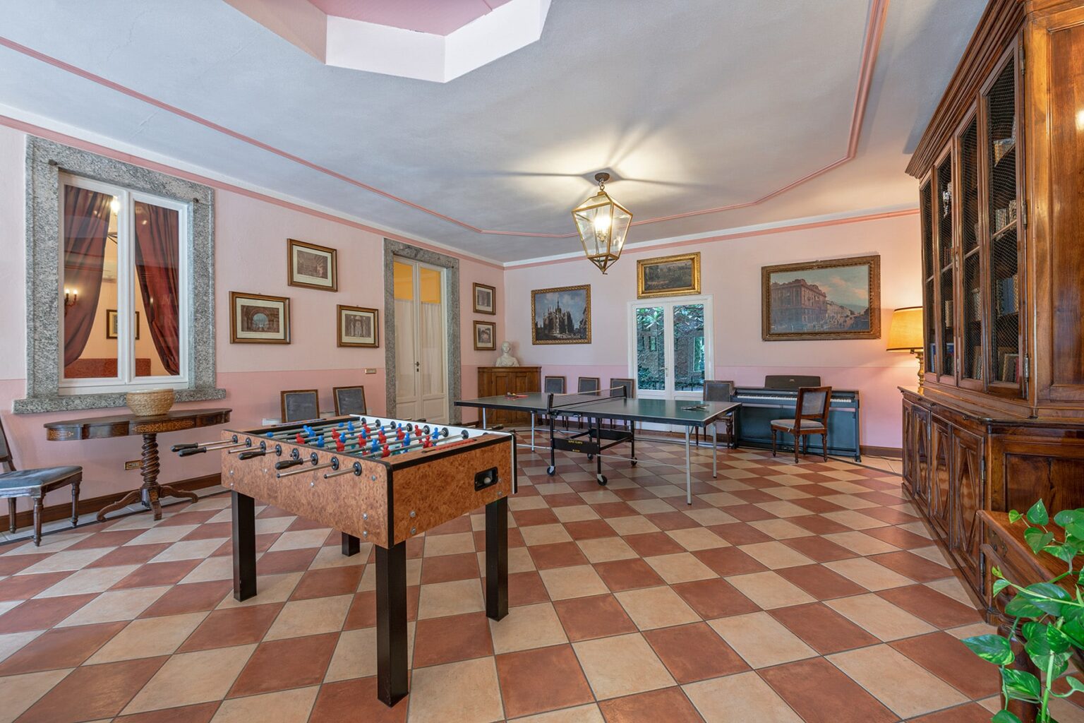 Spacious game room featuring a foosball table, elegant furnishings, and large windows with views, adorned with artwork and a warm color palette. | Only on SopranoVillas
