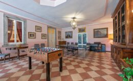 Spacious game room featuring a foosball table, elegant furnishings, and large windows with views, adorned with artwork and a warm color palette.