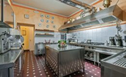 Modern commercial kitchen with stainless steel equipment, spacious island, and decorative plates on the wall, showcasing a clean and organized cooking environment.