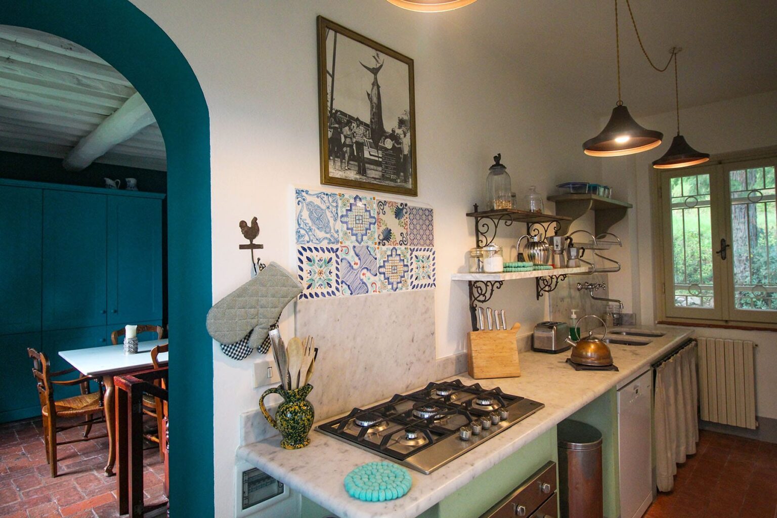Charming kitchen interior featuring a marble countertop, traditional gas stove, vintage decor, and colorful tiles, with natural light streaming in through the window. | Only on SopranoVillas