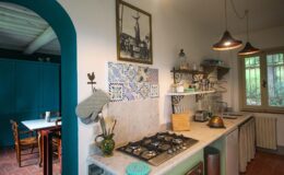Charming kitchen interior featuring a marble countertop, traditional gas stove, vintage decor, and colorful tiles, with natural light streaming in through the window.