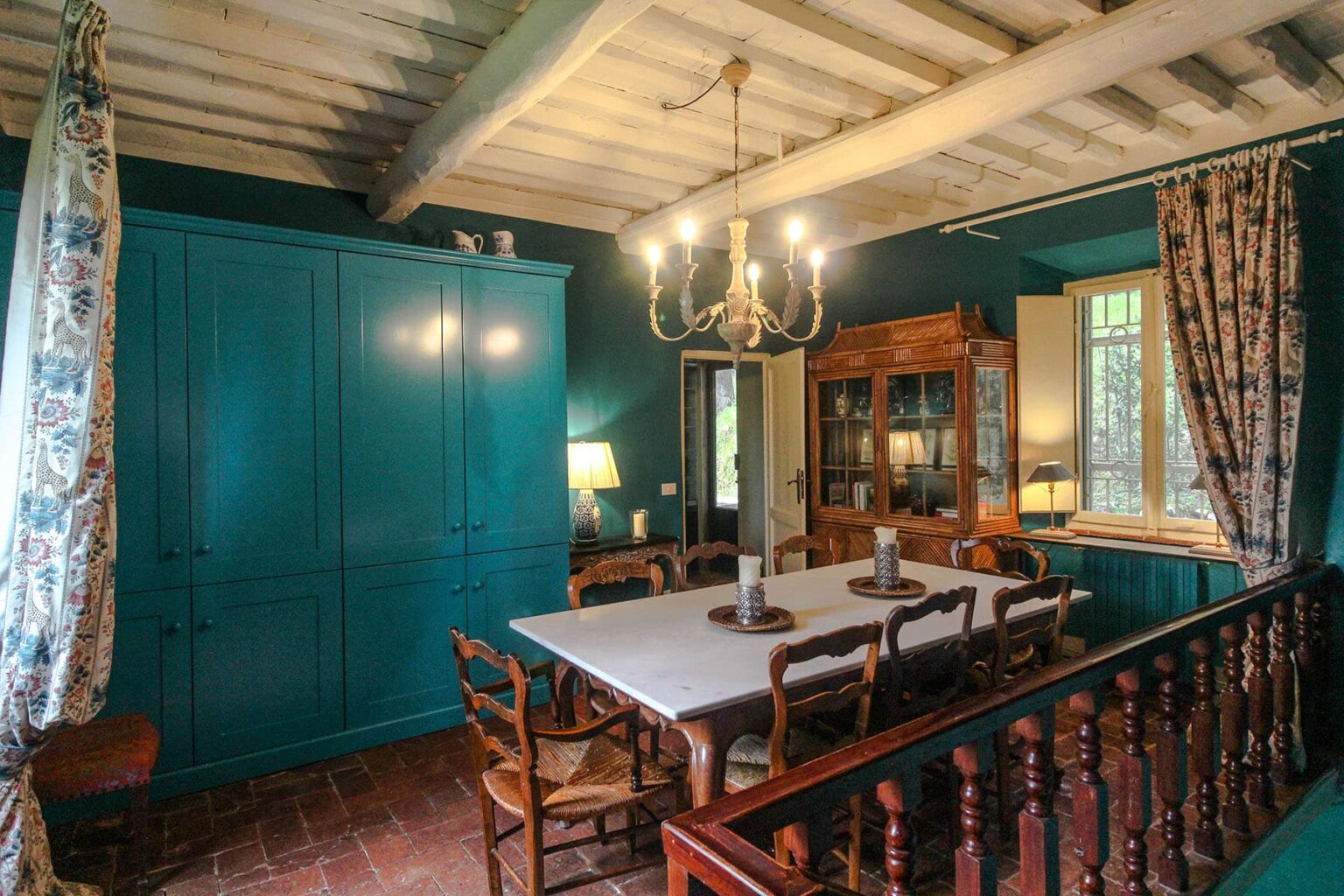 Charming dining room featuring a large wooden table surrounded by rustic chairs, teal walls, and elegant chandeliers, highlighting a cozy and inviting atmosphere. | Only on SopranoVillas