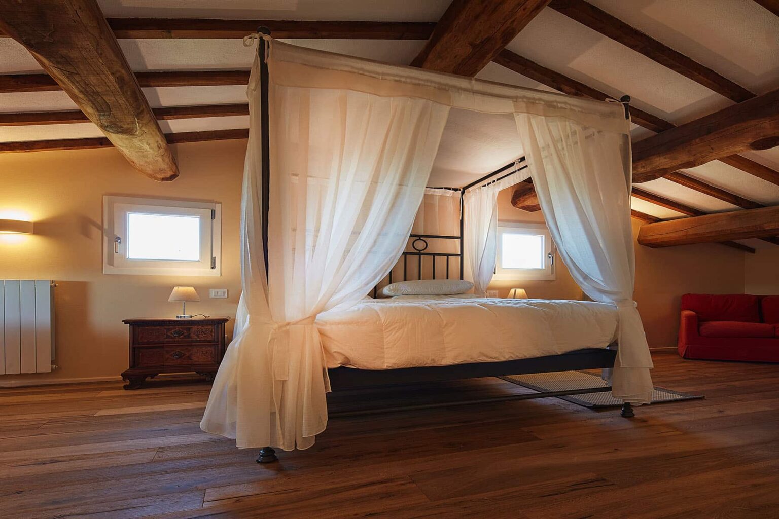 Cozy bedroom featuring a four-poster bed with sheer curtains, wooden beams, and warm lighting, creating an inviting atmosphere in a rustic setting. | Only on SopranoVillas