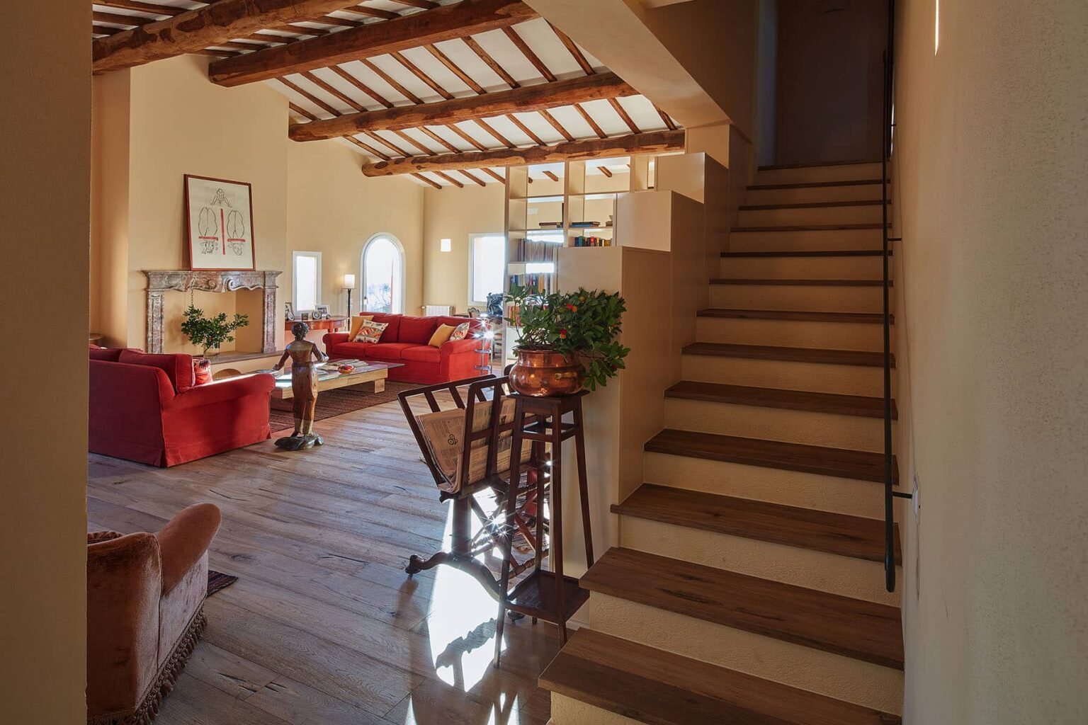 Interior view of a spacious living area featuring red sofas, wooden beams, and a staircase leading to the upper level, showcasing a warm and inviting atmosphere. | Only on SopranoVillas