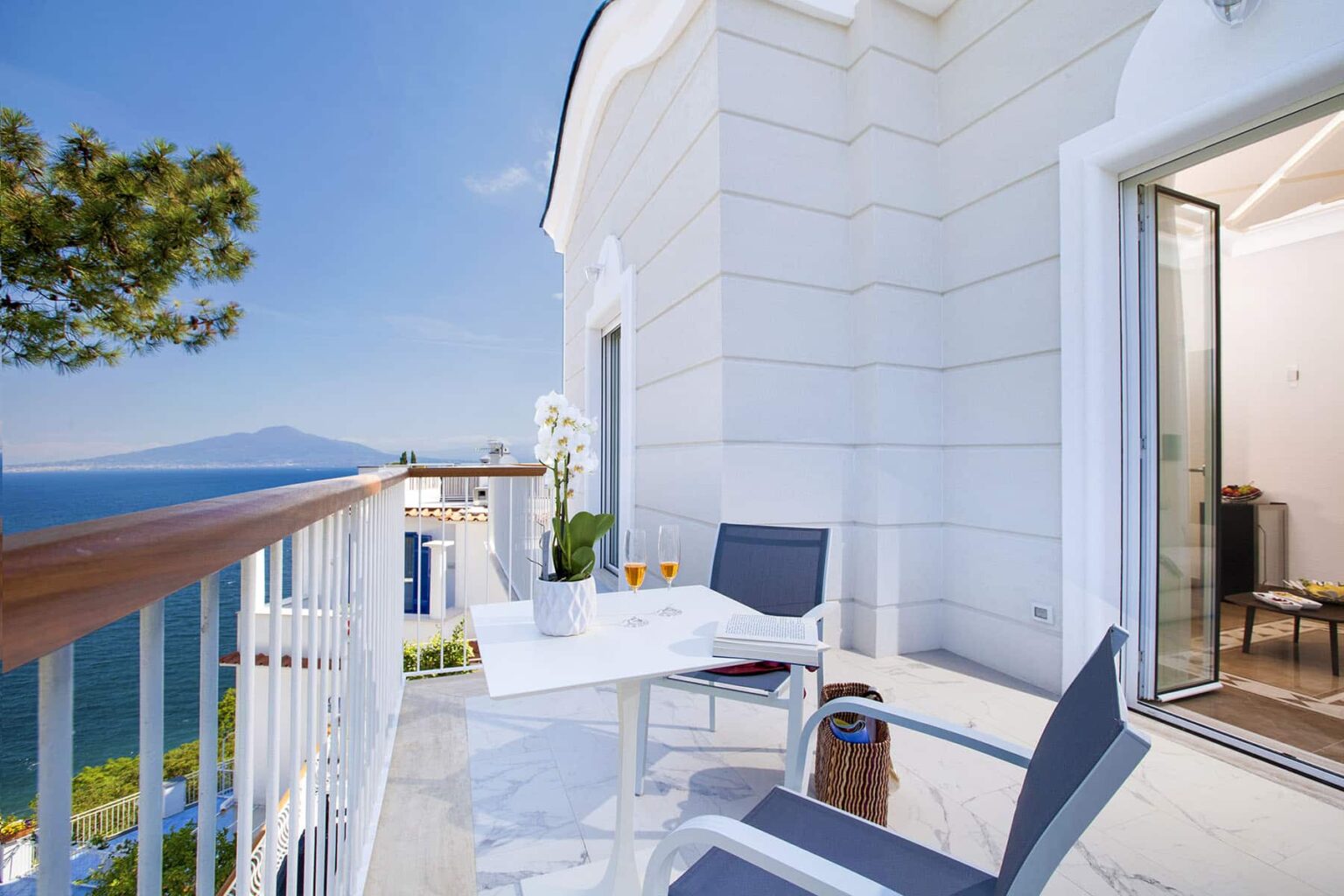 Balcony view overlooking the sea with modern outdoor furniture and a table, featuring a serene atmosphere and bright blue sky. Ideal for relaxation and enjoying scenic vistas. | Only on SopranoVillas