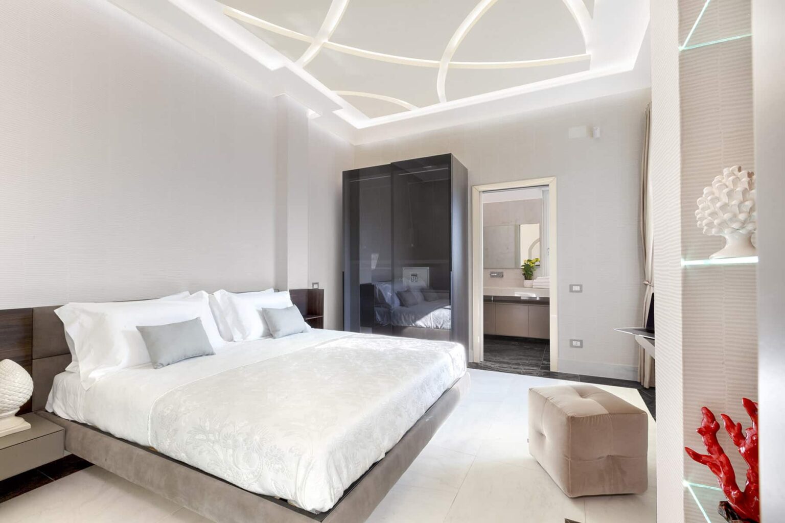 Modern bedroom featuring a large bed with white linens, stylish decor, and ambient lighting. The room includes a sleek wardrobe and a cozy seating area, creating a serene and inviting atmosphere. | Only on SopranoVillas