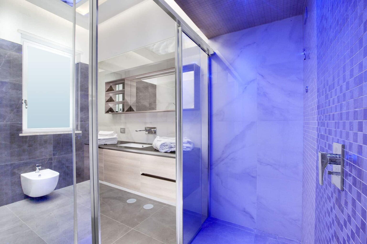Modern bathroom interior featuring a sleek glass shower, minimalist design, and contemporary fixtures. The space is illuminated with soft lighting, showcasing gray tiles and a stylish vanity. | Only on SopranoVillas