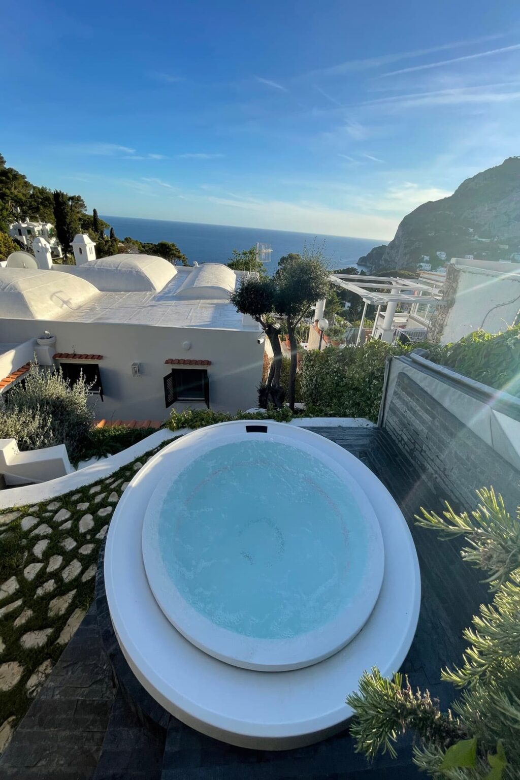 Scenic view of a private hot tub overlooking the ocean, surrounded by lush greenery and modern architecture, ideal for a luxurious getaway. | Only on SopranoVillas