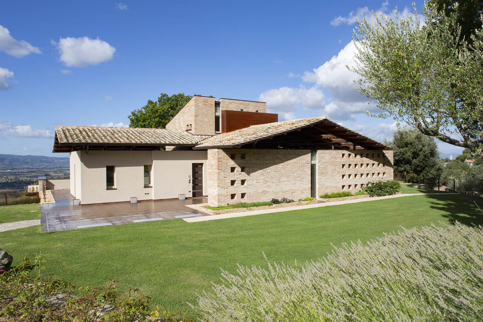 Modern architectural design of a house with a stone facade and a sloped roof, surrounded by green lawn and trees under a clear blue sky. | Only on SopranoVillas