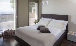 Modern bedroom featuring a comfortable queen-sized bed with neutral bedding, decorative pillows, and a minimalistic design. Natural light streams in through large windows, enhancing the serene atmosphere. The room includes a bedside table and a cozy seating area, ideal for relaxation.