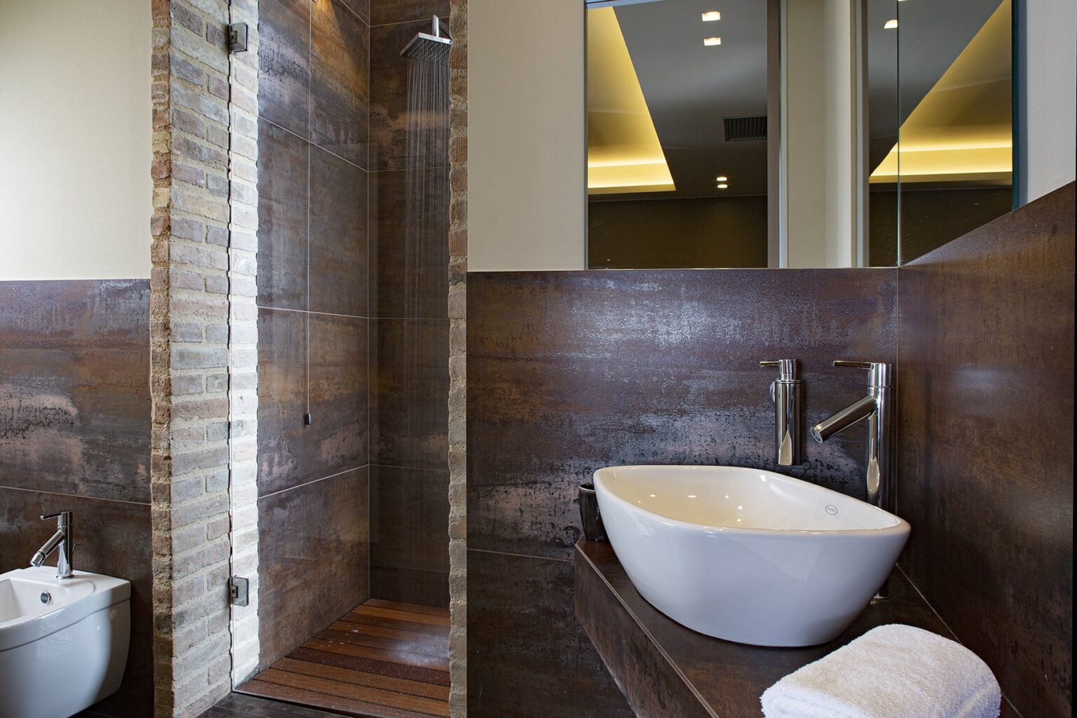Modern bathroom interior featuring a stylish walk-in shower with natural stone walls, a contemporary white sink, and elegant wooden accents. Bright lighting enhances the spacious design, creating a relaxing atmosphere. | Only on SopranoVillas