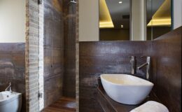 Modern bathroom interior featuring a stylish walk-in shower with natural stone walls, a contemporary white sink, and elegant wooden accents. Bright lighting enhances the spacious design, creating a relaxing atmosphere.