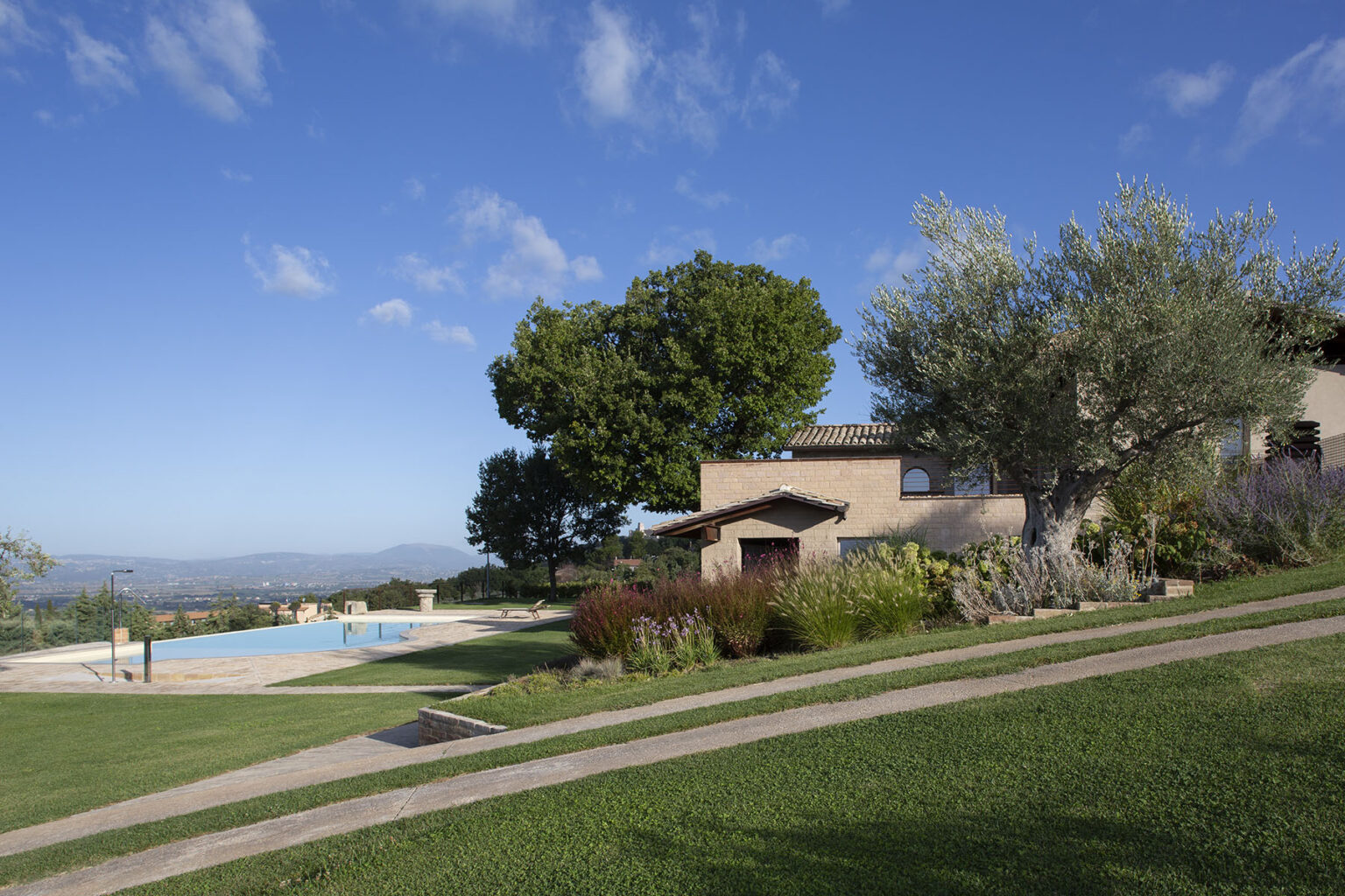 Scenic view of a hillside villa with a swimming pool, surrounded by lush greenery and trees under a clear blue sky. Ideal for luxury vacation rentals or countryside retreats. | Only on SopranoVillas