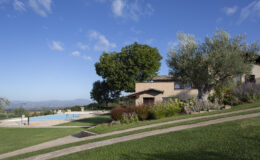 Scenic view of a hillside villa with a swimming pool, surrounded by lush greenery and trees under a clear blue sky. Ideal for luxury vacation rentals or countryside retreats.