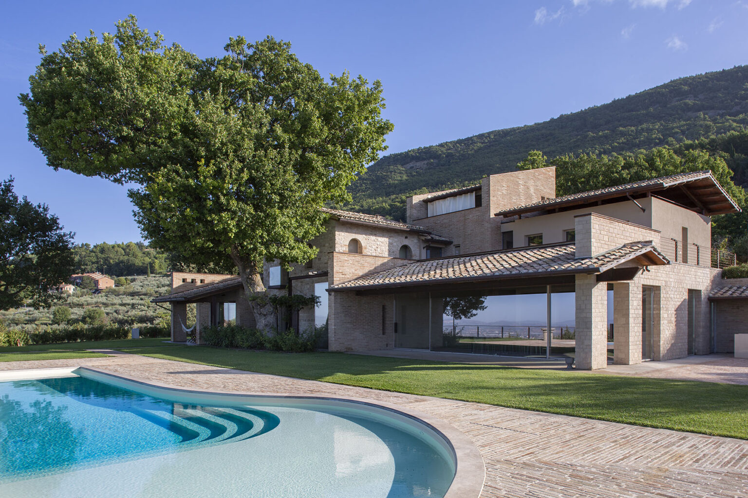 Modern architectural home with a swimming pool, surrounded by lush greenery and mountains, showcasing a blend of natural materials and contemporary design. | Only on SopranoVillas