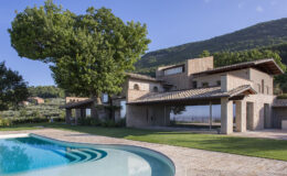 Modern architectural home with a swimming pool, surrounded by lush greenery and mountains, showcasing a blend of natural materials and contemporary design.