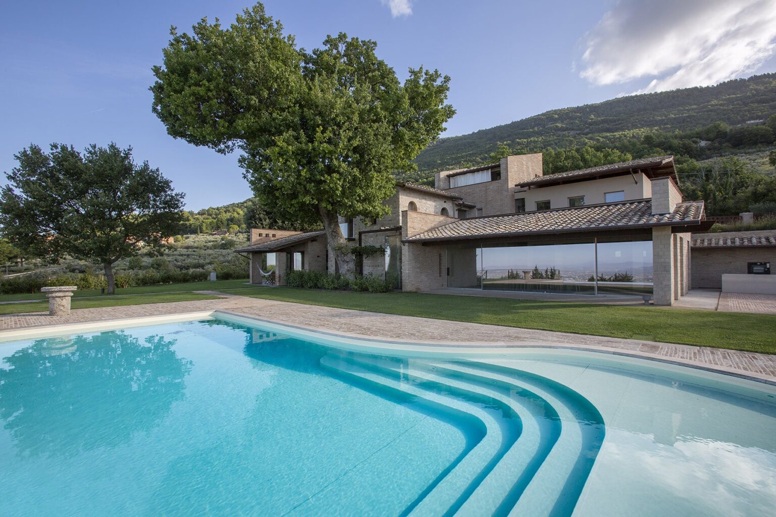 Modern villa with a swimming pool, surrounded by lush greenery and mountains, showcasing a serene outdoor living space. | Only on SopranoVillas