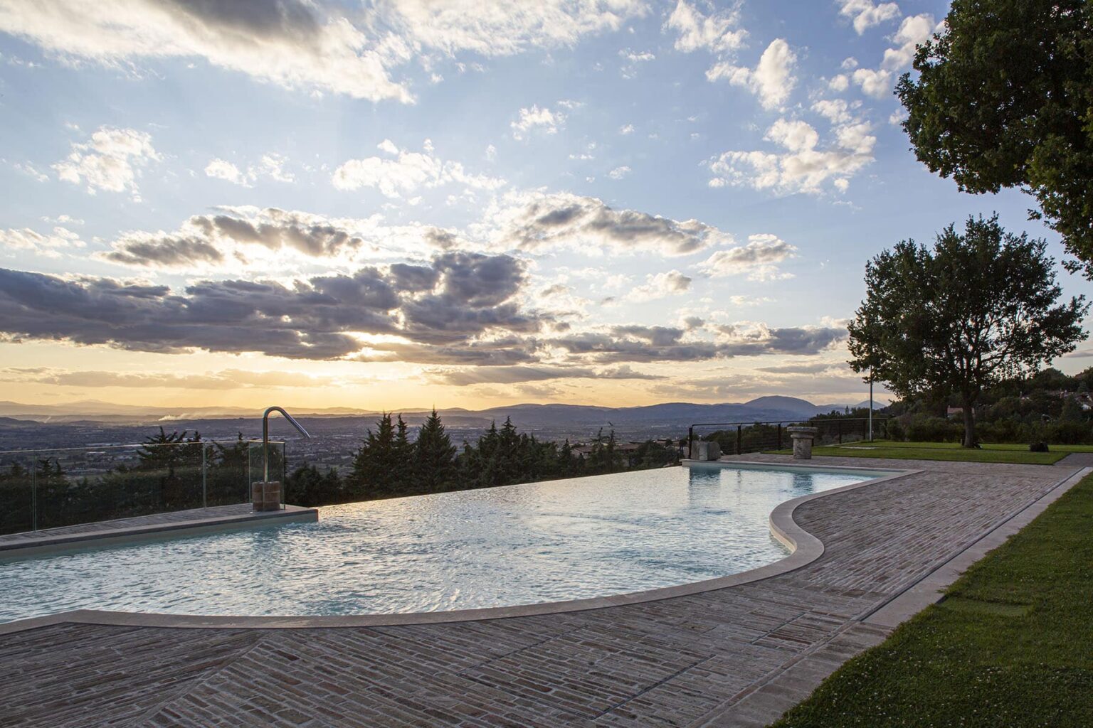 Scenic outdoor swimming pool with a stunning sunset view, surrounded by lush greenery and distant mountains. | Only on SopranoVillas