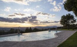 Scenic outdoor swimming pool with a stunning sunset view, surrounded by lush greenery and distant mountains.