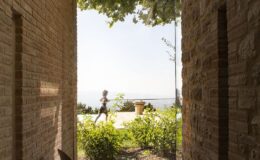 A person jogging through a stone archway with a view of lush greenery and a distant landscape under a clear sky, showcasing an outdoor lifestyle and architectural design.