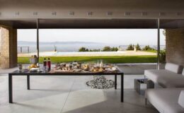 Modern outdoor dining area featuring a stylish table set with an array of gourmet food and beverages, overlooking a scenic landscape with a swimming pool and lush greenery. Ideal for entertaining guests in a luxurious setting.