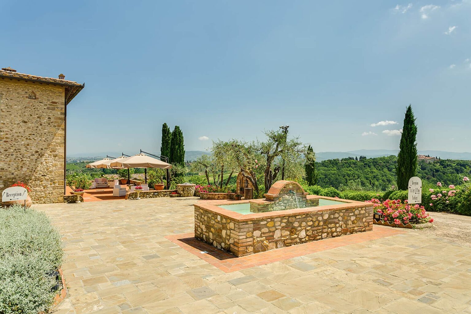 Scenic view of a stone patio with a water feature, surrounded by lush greenery and cypress trees, showcasing a tranquil outdoor space in Tuscany. | Only on SopranoVillas