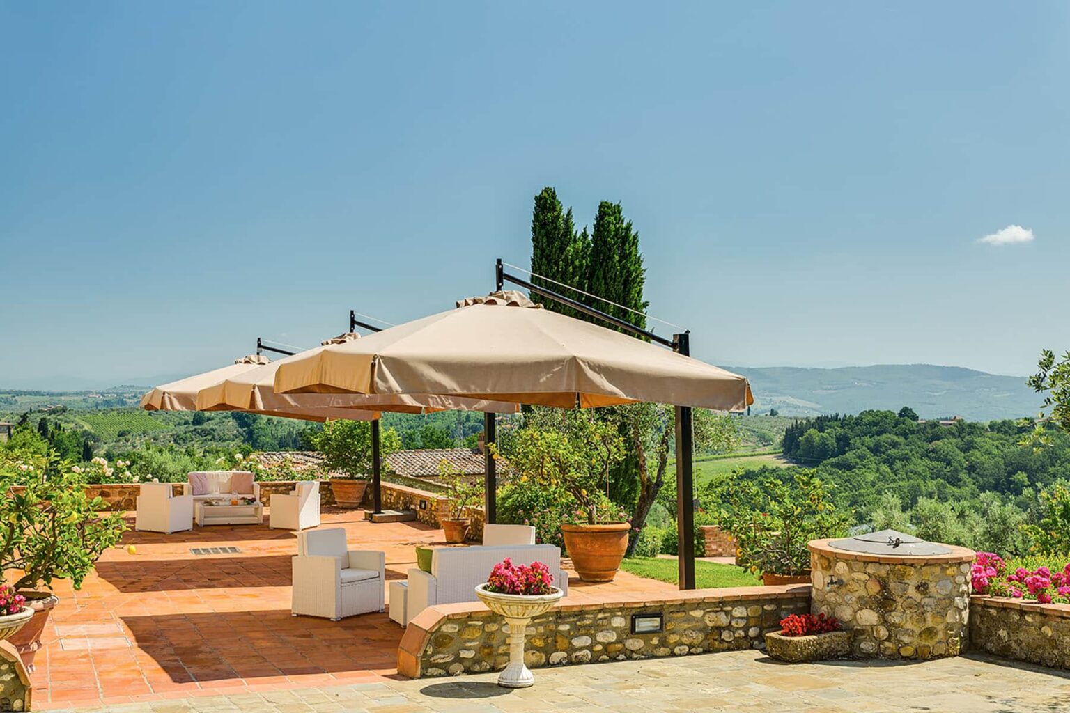 Scenic outdoor patio with shaded seating areas and potted plants, overlooking lush green hills and a clear blue sky. Ideal for relaxation and enjoying nature. | Only on SopranoVillas