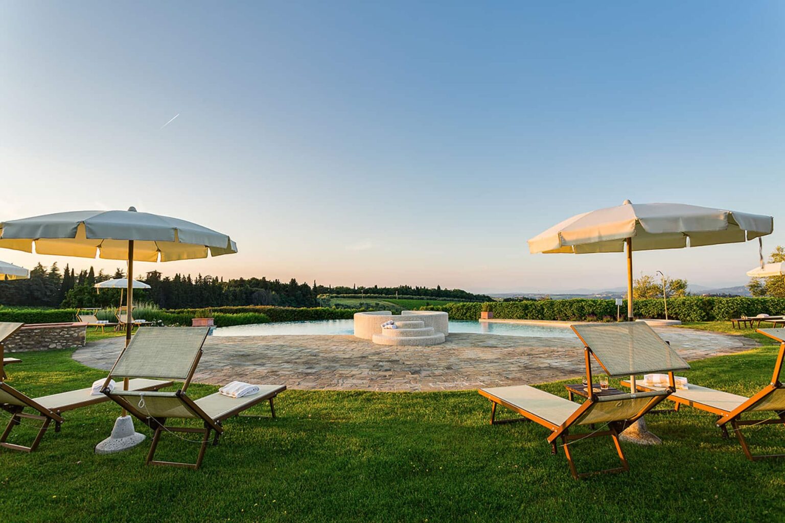 Serene outdoor pool area with lounge chairs and umbrellas, surrounded by lush greenery and a clear blue sky, perfect for relaxation and leisure. | Only on SopranoVillas