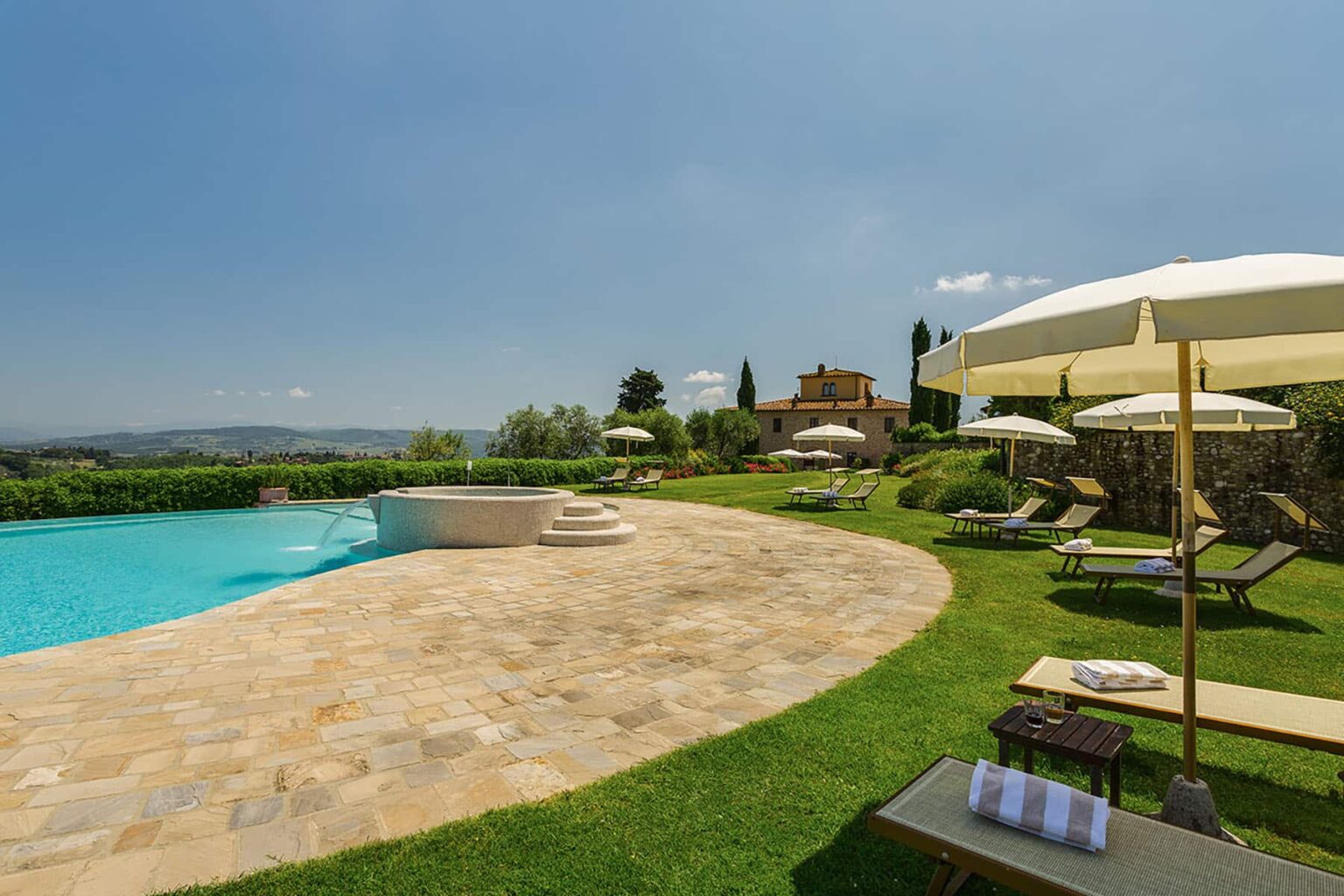 Luxurious outdoor pool area featuring sun loungers and umbrellas, surrounded by lush greenery and scenic views, ideal for relaxation and leisure. | Only on SopranoVillas