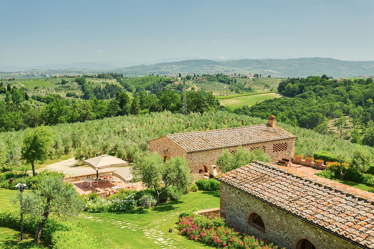 Scenic view of a rustic farmhouse surrounded by lush green hills and olive trees in the Italian countryside, showcasing a serene landscape ideal for relaxation and rural tourism. | Only on SopranoVillas